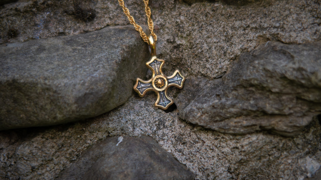 Gold and silver cross pendant on a chain against a stone wall background