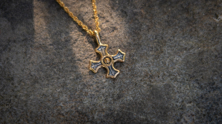 Gold and silver cross pendant on a textured dark background