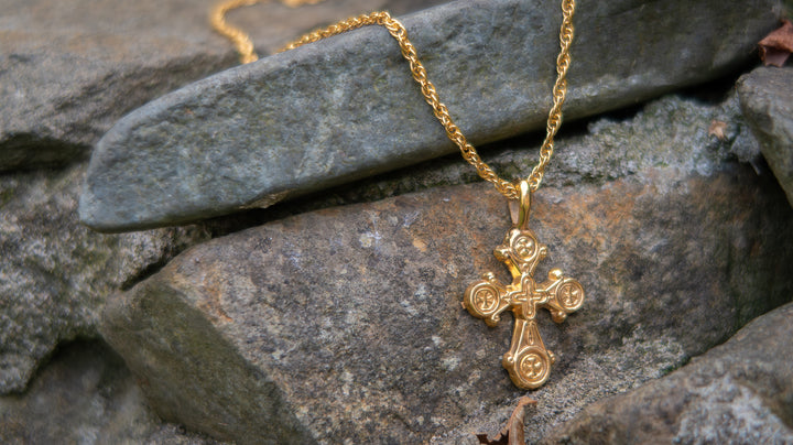 Gold necklace with a cross pendant on a stone surface