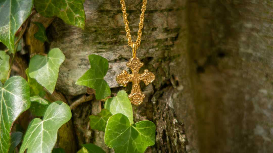 Gold cross necklace against a tree
