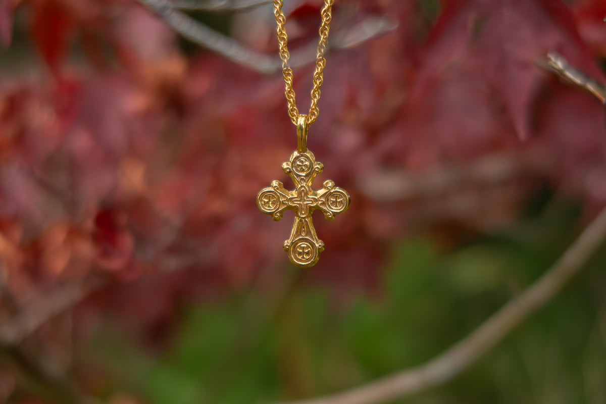 Gold cross necklace against a blurred natural background