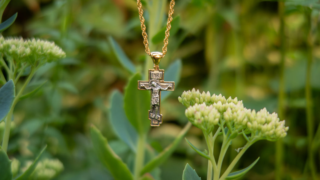 Gold necklace with a cross pendant hanging among green plants