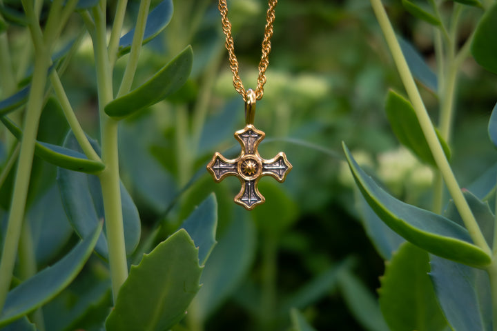 Gold cross pendant necklace on a green leafy background