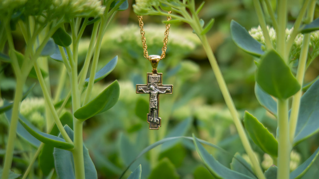 Gold necklace with a cross pendant hanging among green plants