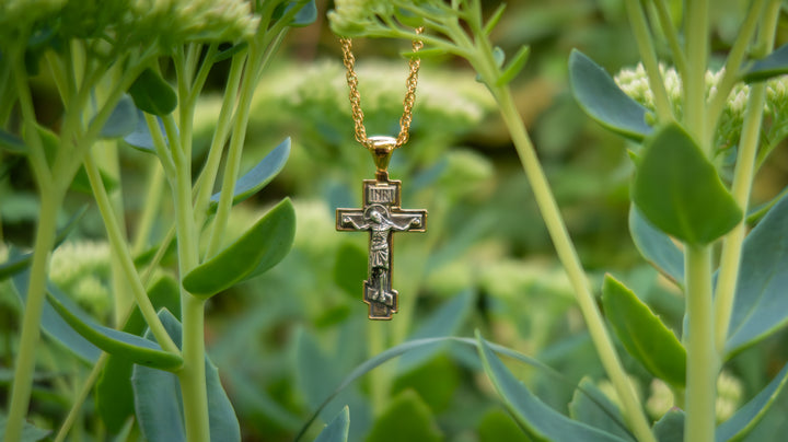 Gold necklace with a cross pendant hanging among green plants