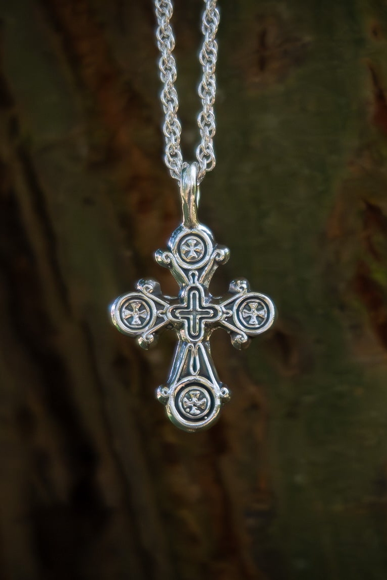 Silver cross pendant on a chain against a tree bark background