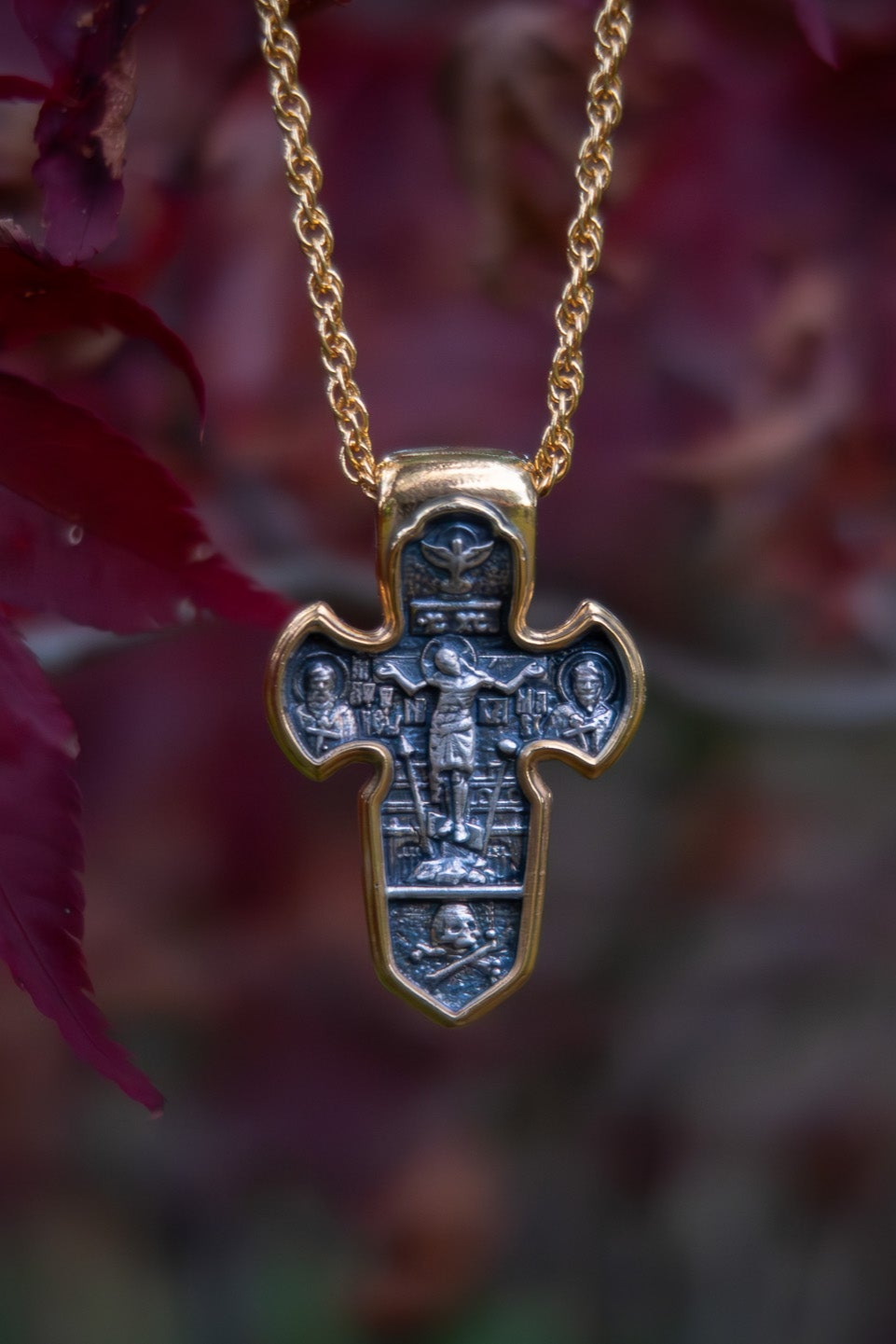 Gold cross pendant with intricate design on a blurred floral background
